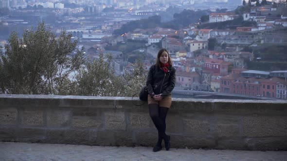 Girl leaning on a stone wall looks at camera, Porto in the background