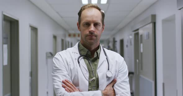 Portrait of caucasian male doctor with arms crossed standing in the corridor at hospital