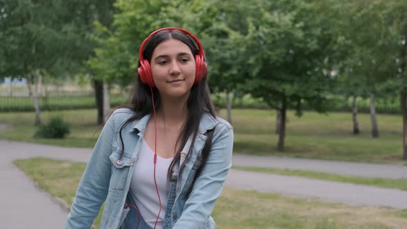 Beautiful Cheerful Girl Dancing in the Park Listening To Music on Headphones. Fun Mood