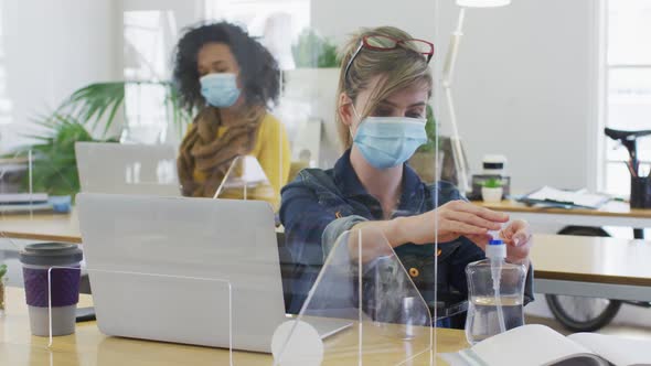 Woman wearing face mask sanitizing her hands at office