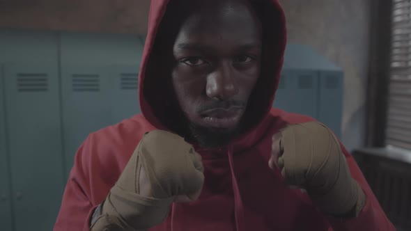 Young Black Fighter in Hoodie, with Clenched Fists Posing in Locker Room