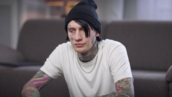 Medium Shot of Young Tattooed Man Looking at Camera Thinking Sitting at Home Indoors