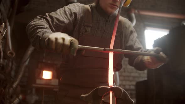 A Man Blacksmith Putting an Iron Detail Between the Clamps and Spinning It Around