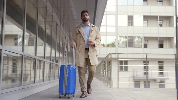 Slider Shot of Man with Suitcase Drinking Coffee Walking Outside Airport