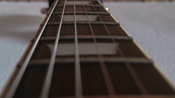 Neck of a les paul electric guitar that is hanging off a white wall. Handheld close-up tracking shot