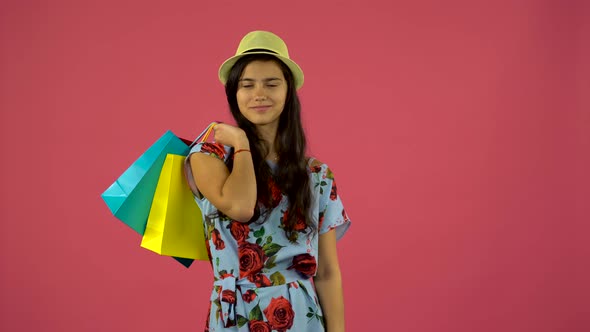 Shopaholic Girl with Bags in Her Hands Is Standing and Starts Smiling, Pink Background