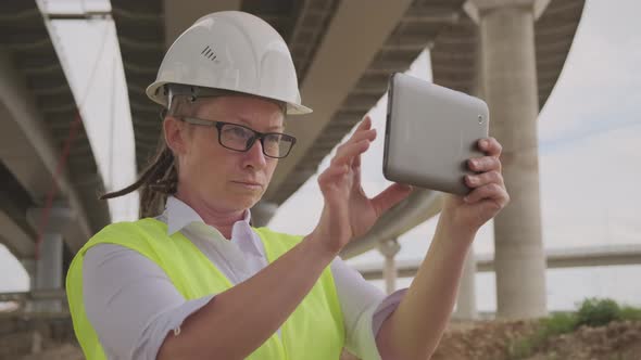 Serious female engineer or inspector in white hard hat working on tablet computer