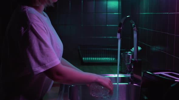 Woman Opens Crane with Water in Modern Kitchen with Neon Light and Washing Dirty Glass.