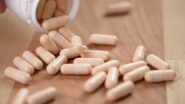 Vitamin B capsules fall from a white plastic container on a wooden eco surface