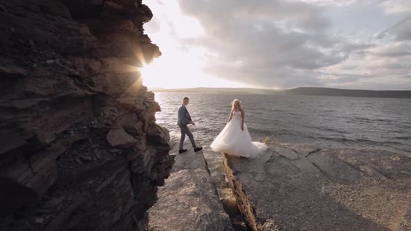 Groom Goes To Bride and Gives Her a Hand. Newlyweds on Mountainside By the Sea