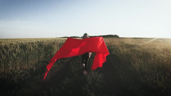 Young Girl Running with Red Tissue in Green Field. Happy Cute Girl Playing in the Wheat Field on a