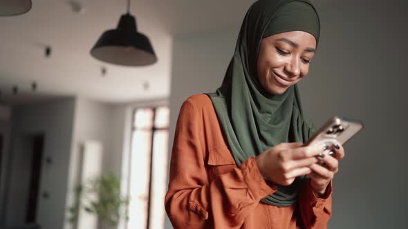 Smiling Muslim woman typing by phone