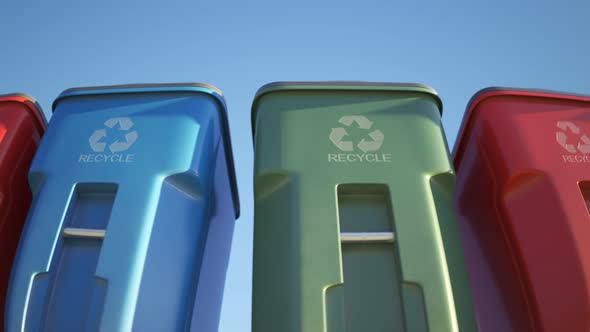 Colorful plastic garbage bins stacked in a row against a clear sky background.