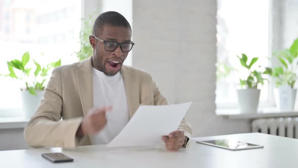 African Man Celebrating Success While Reading Documents in Office