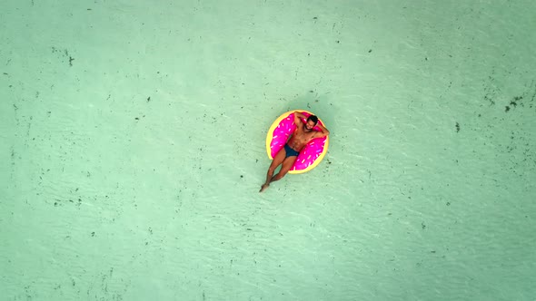 Aerial view of man floating on inflatable donut mattress, relaxing.