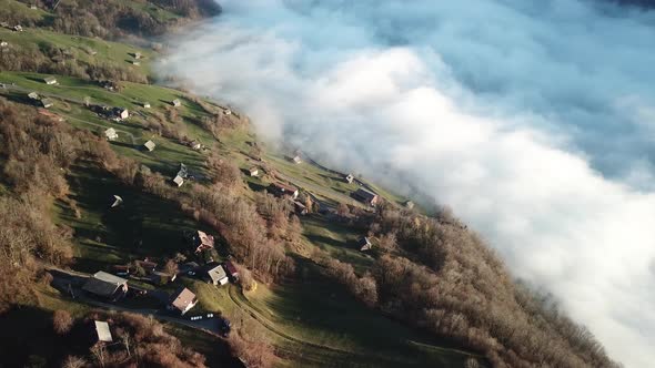 Small village on the slope of a mountain range with low hanging clouds of fog in the valley. Smooth