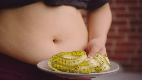 Female Hands Hold Plate with a Measuring Tape Against the Background of a Large Belly