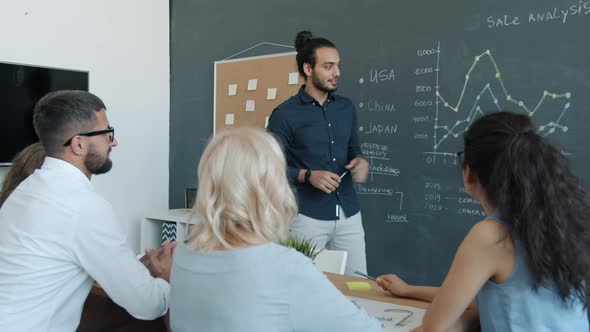 Cheerful MiddleEastern Man Making Presentation for Multiethnic Group of Colleagues in Shared Office