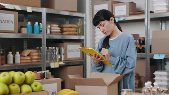 Woman with Clipboard in Hands Volunteering at Warehouse