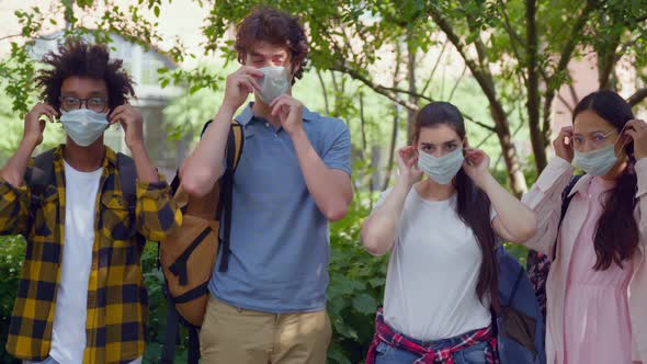 Portrait of Multiethnic Students Put on Safety Mask Looking at Camera Outdoors