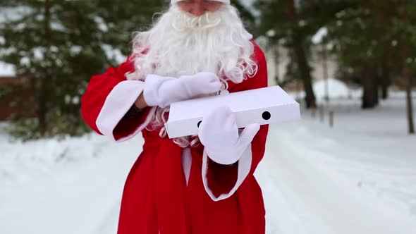 White pizza box open in hands of Santa Claus in white mittens, with beard, in a red coat. Christmas