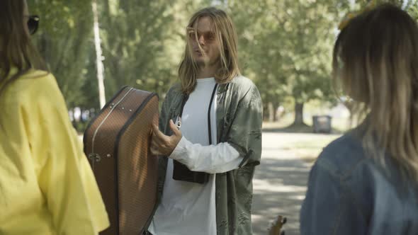 Joyful Hippie Man Sunglasses Walking Suitcase Talking To Women Outdoors