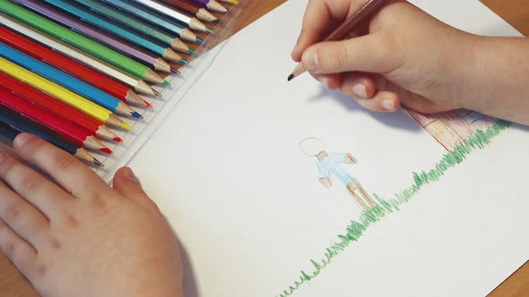 Childrens Hands Draw a Man Near the House with a Pencil Closeup