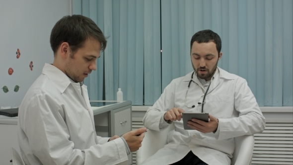 Two Male Doctors At Medical Cabinet Using Mobile Phones