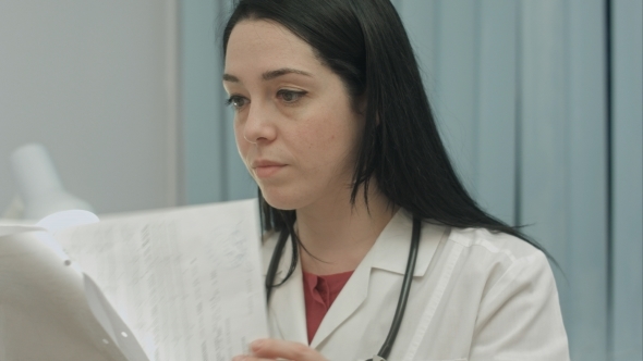 Female Doctor In Medical Office Analyzes Results An Electrocardiogram And Takes Notes