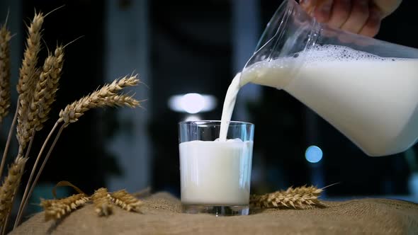 A Man Pours Milk From A Jug Into A Glass On A Rustic Background, A Natural Dairy Product