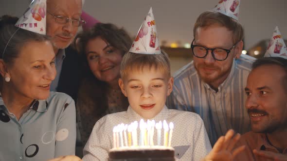 Cute Boy Blowing Out Birthday Cake Candles at Family Party