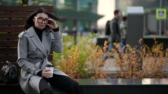 Elegant Lady is Sitting on Bench in Park and Drinking Coffee From Cardboard Cup