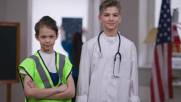 Two Confident Teenage Boys in Builder and Doctor Uniform Looking at Camera Smiling Gesturing