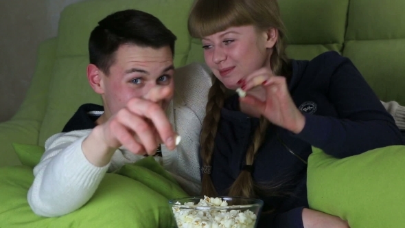 Young Couple With Popcorn Watching Comedy On Television And Laugh