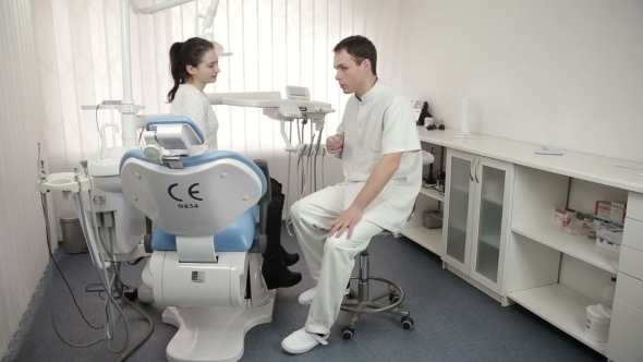 Young Dentist Talking To Beautiful Female Patient Of The Dental Office