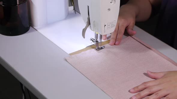 Sewing machine being used to stitch entire side of pink and white colored fabric