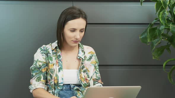 Smiling woman using laptop sitting on floor in living room. Female working from home