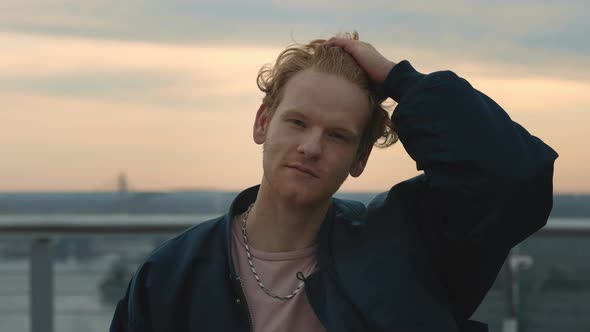 Portrait of Handsome Young Man Adjusting Curly Red Hair During Strong Wind on Street