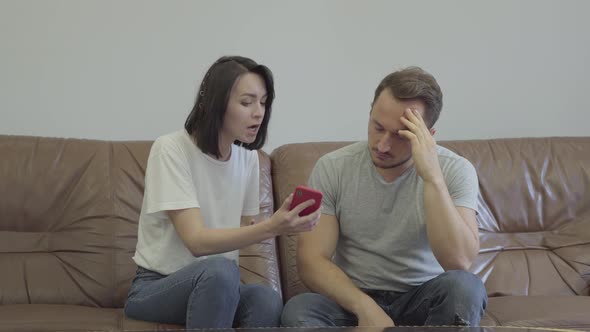 Portrait of Angry Woman Shouting at Her Sad Husband Showing Cellphone with Messages