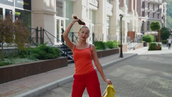 a Blonde in Red Clothes Holds Tail with One Hand and a Yellow Jacket with the Other on a City Street