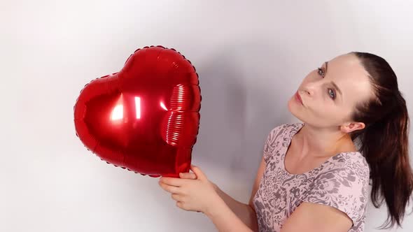 An attractive young female model wearing a cute flowery dress holding a heart shaped balloon