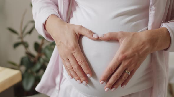 Woman Holding Hands on Pregnant Belly in Heart Shape