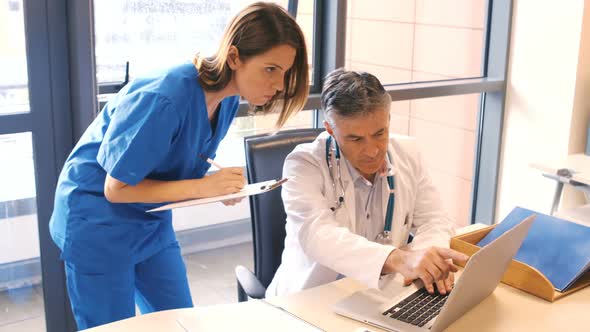 Doctor using laptop while nurse writing on clipboard