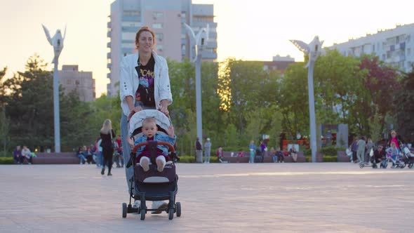 Caucasian Woman Walking Along the Alley in Summer Park with Baby Stroller