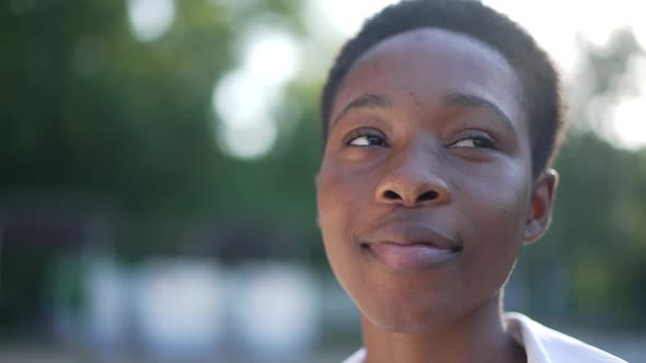 Headshot Portrait of Young African American Woman in Sunrays Looking Around Smiling