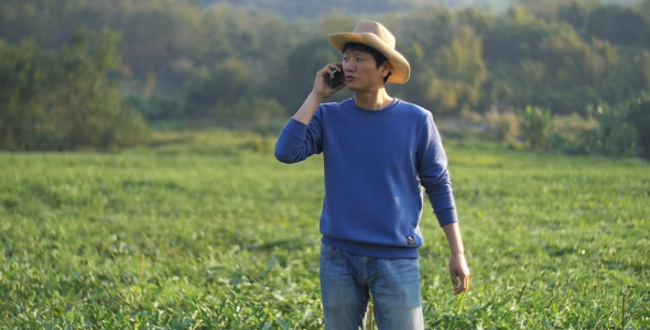 Asian Farmer In A Field Talking On Phone