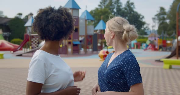 Medium Shot of Multiethnic Young Women Talking and Watching Children Play on Playground