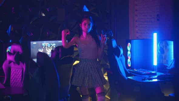 Young Sexy Daring Woman with Ponytail Holding a Joystick in Neon Gaming Club and Blows a Bubble Gum