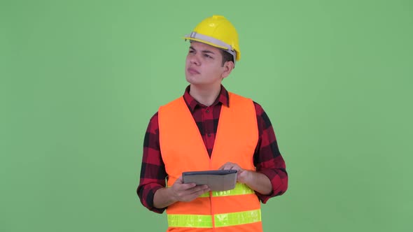 Happy Young Multi Ethnic Man Construction Worker Thinking While Using Digital Tablet