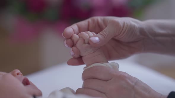 Closeup Female Caucasian Hand Caressing Fist of Newborn Crying Girl Indoors